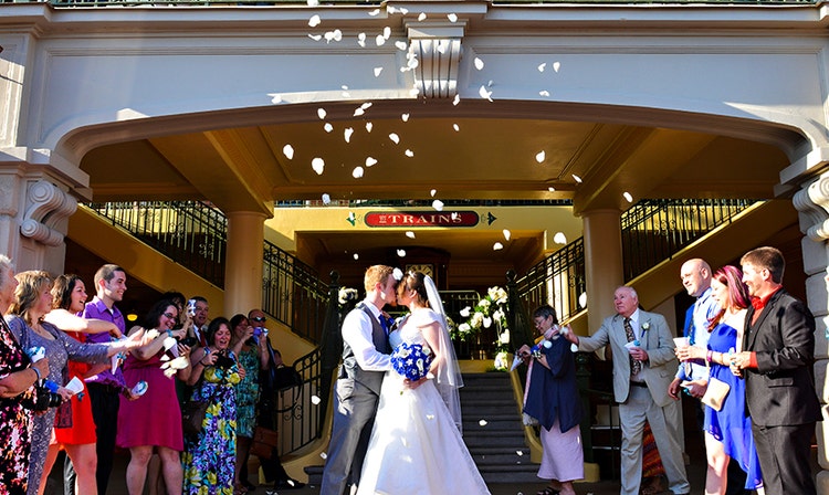 People cheer as a bride and groom kiss in front of a train station
