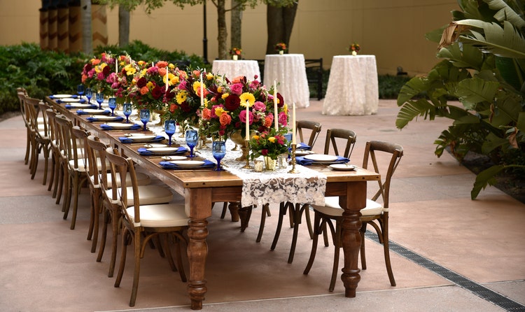 A long table with many place settings on a courtyard with 3 table tops in the background