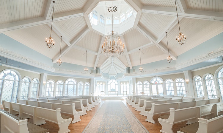 A chapel and altar in Disney’s Wedding Pavilion with several chandeliers, a wide aisle and 2 sides of pews