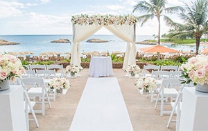 Two pillars holding rose bouquets line an aisle leading towards an altar outside