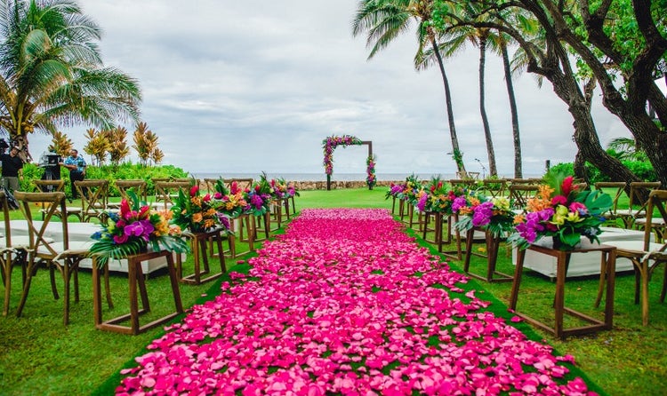 A walkway covered with flowers alongside rows of chairs leading to an arch overlooking Lanikuhonua