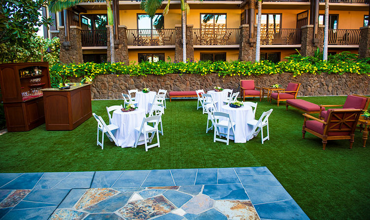 A fancy setting of dining and cocktail tables in front of a mosaic on the lawn of a resort