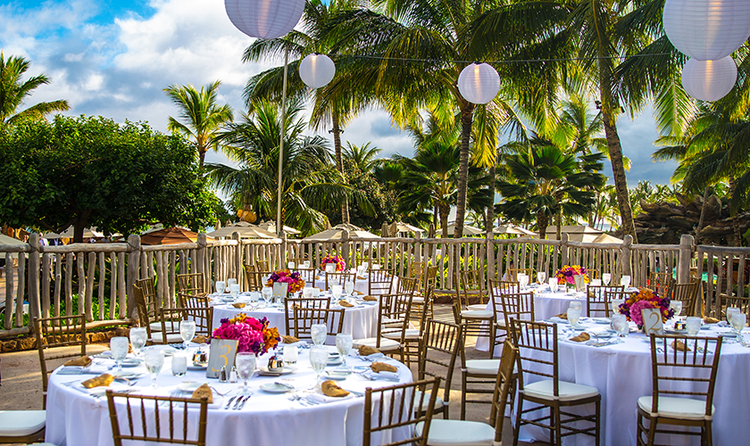 A wedding reception on an outside patio holding several round tables with floral centerpieces and place settings