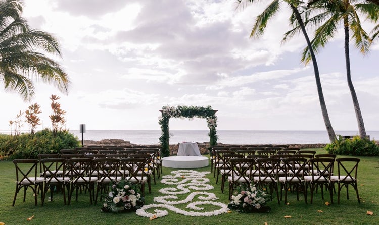 Chairs lined up in front of an arch overlooking Lanikuhonua beach and surrounded by palm trees