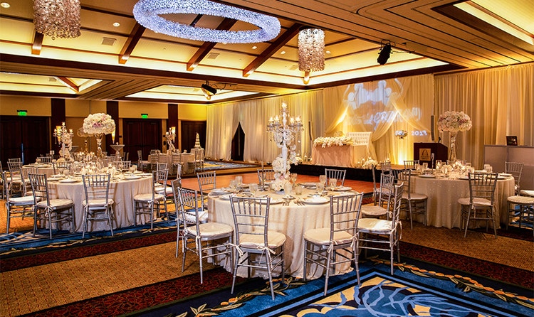 Several tables with place settings and a dance floor in a room decorated with large bouquets of flowers