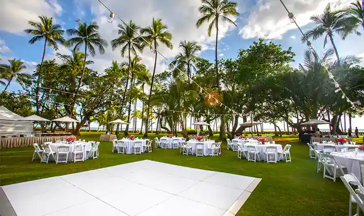 Strings of lights extending over a dance floor on a lawn surrounded by palm trees