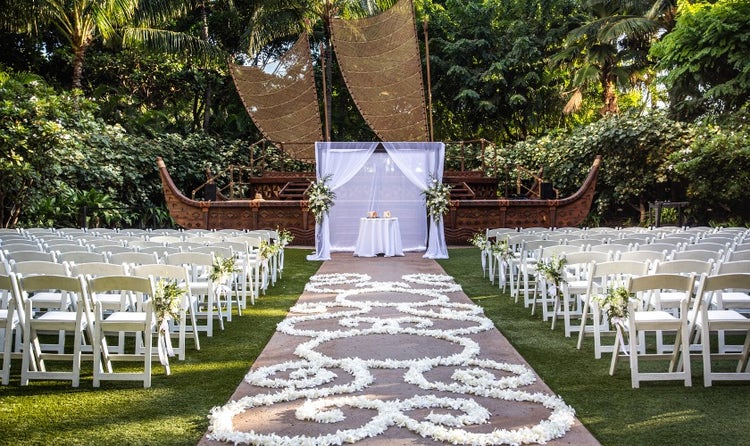 Rows of chairs along an aisle covered with flower petals leading to a table in front of a stage