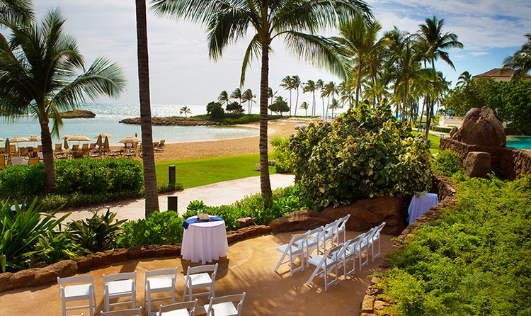 The Sunset Alcove by the beach at Aulani Resort set for a wedding ceremony with 2 rows of folding chairs facing a cloth covered table at the front