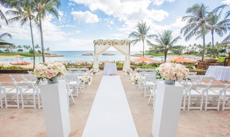 A walkway leading past chairs to a table beneath a canopy overlooking the ocean and palm trees