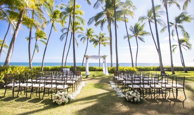 Chairs lined up in front of an arch overlooking Lanikuhonua beach and surrounded by palm trees