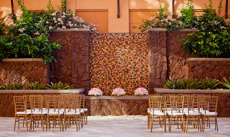 Two groups of wedding seating in a resort courtyard with a stone wall