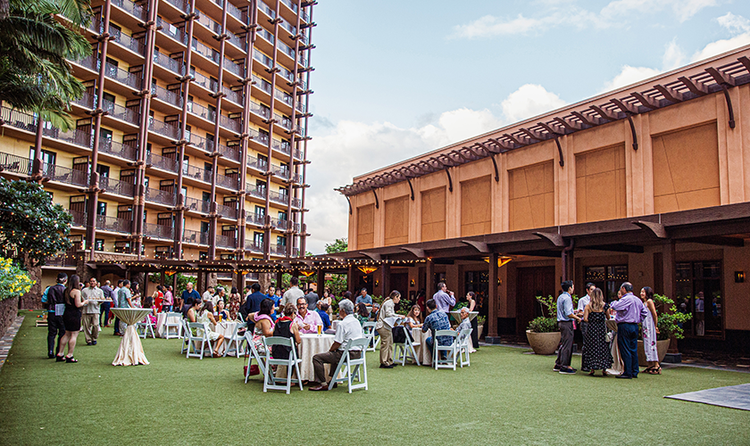 Guests in Aloha attire, interacting at a wedding in a courtyard at Aulani, a Disney Resort and Spa