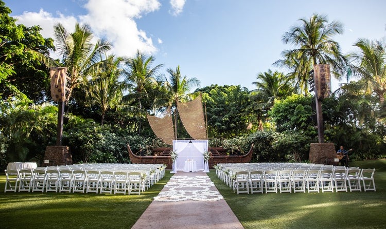 Rows of chairs along an aisle covered with flower petals leading to a table in front of a stage
