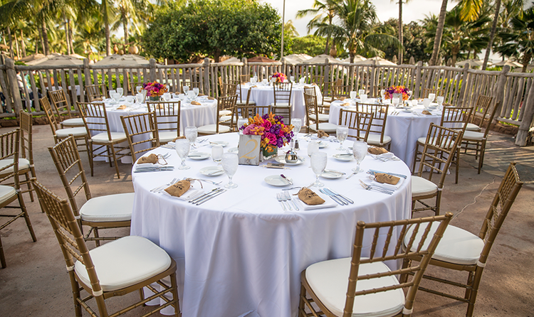 Four round tables with floral centerpieces arranged on a patio