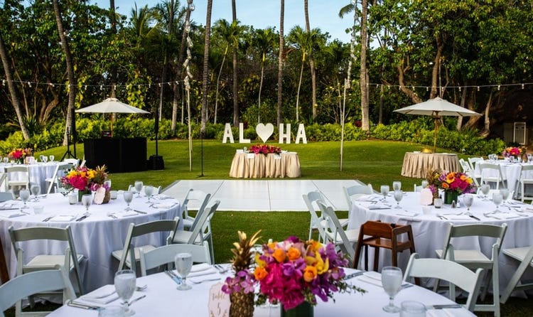 Chairs and tables set up on a lawn featuring a D J booth and string lights