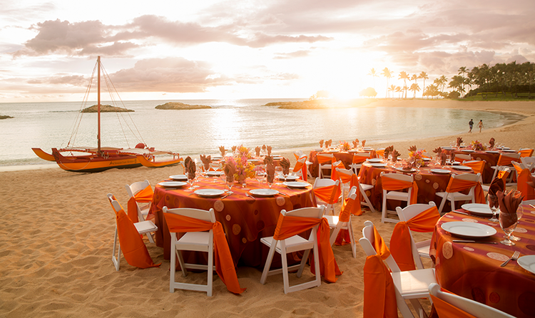 The sun sets over a wedding reception on a beach