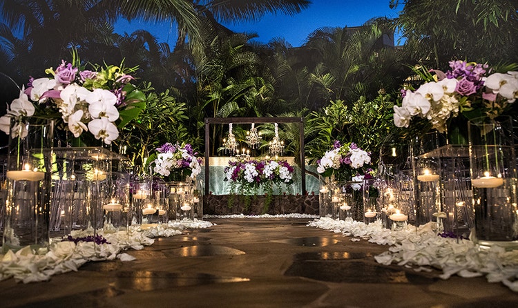 Several lit candles line an aisle along with several bouquets of flowers