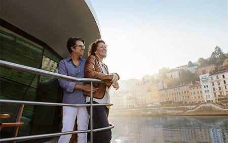 Newlyweds leaning against a boat railing while taking in historic buildings during a European river cruise