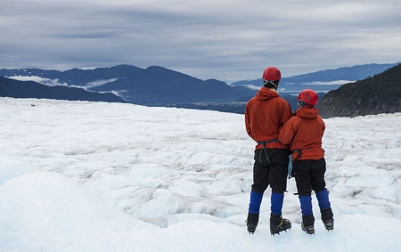 Newlyweds embracing on an ice field with snowcapped mountains in the distance in Alaska