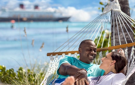 A newlyweds in a beach hammock with a Disney cruise ship in the distance
