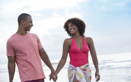 A newlyweds smiling and holding hands as they walk along the ocean on a shoreline