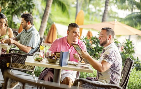 Newlyweds smiling and looking at menus while dining outdoors during their honeymoon at Aulani, a Disney Resort & Spa