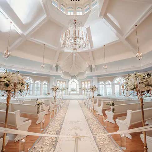 The interior of Disney's Wedding Pavilion at Disney's Grand Floridian Resort & Spa, with pews, a vaulted ceiling and a large chandelier