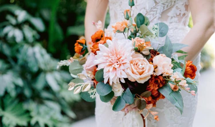 A bride in a lace gown holding a bouquet of dahlias and ranunculus