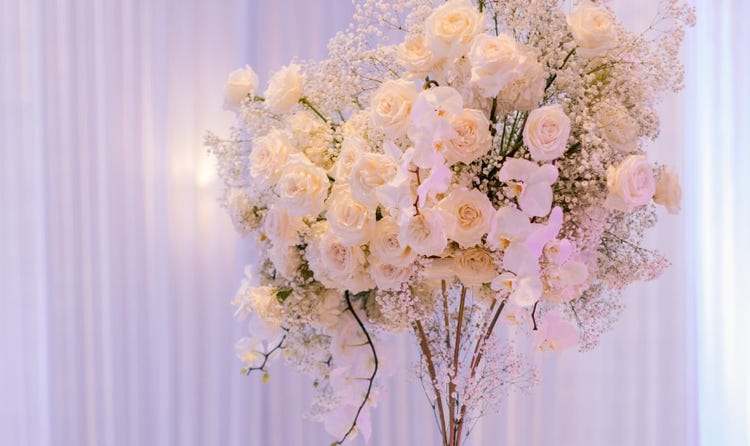 A towering centerpiece of roses, orchids and baby's breath over a set reception table with place settings