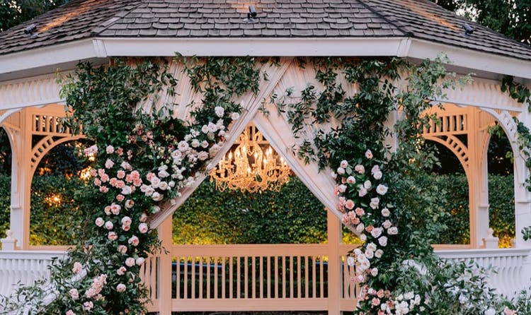 A wedding gazebo draped in roses and greenery, lit by a crystal chandelier and candles