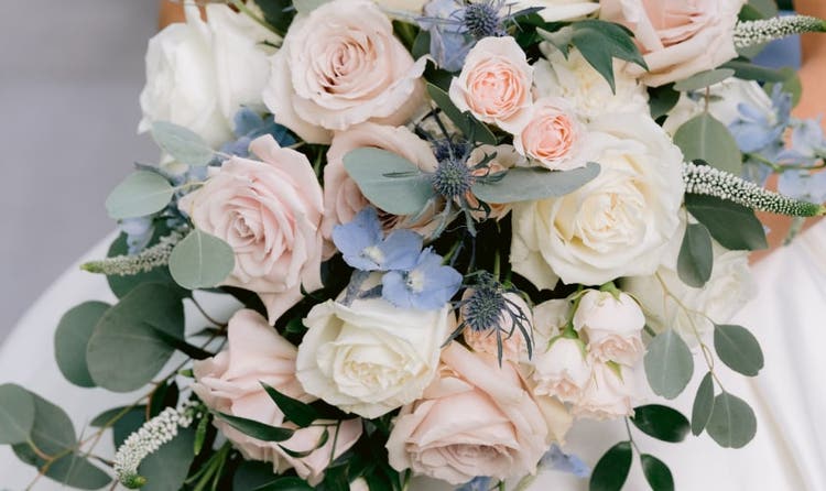 A bride in an off the shoulder gown holding a cascading bouquet of roses and wildflowers