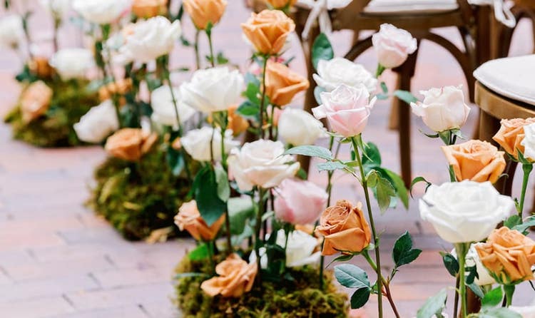 Roses planted in moss next to chairs lining a brick ceremony aisle