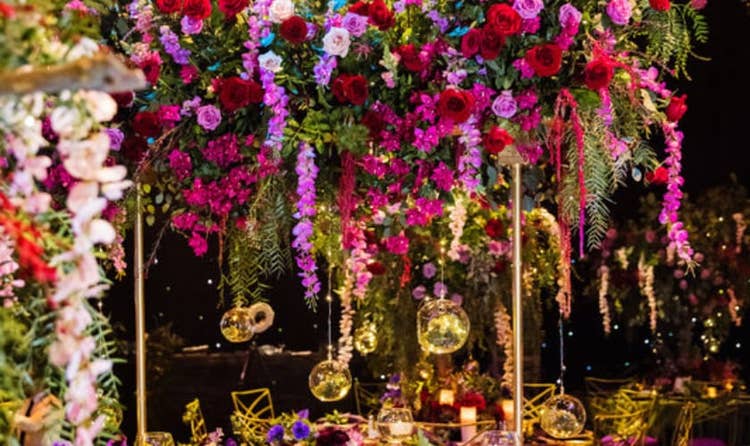 A wedding reception table with a towering centerpiece of roses and hanging globe lights