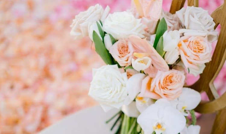 A bridal bouquet of roses, orchids and trailing greenery resting on a ceremony chair