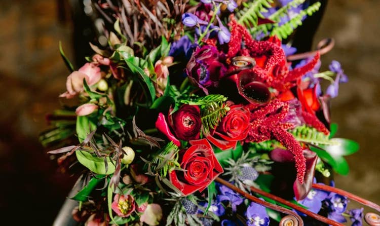 A dramatic wedding bouquet of deep roses, calla lilies, delphiniums and wild greenery