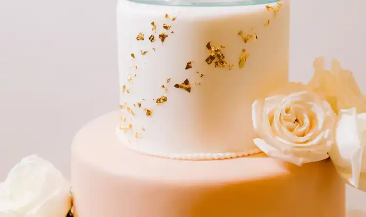 A 2 tier wedding cake with a glass cake topper featuring a couple
