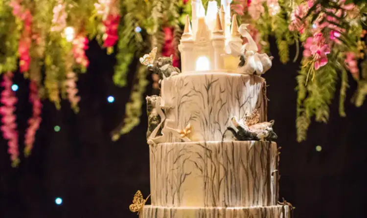 A 4 tier wedding cake decorated to resemble an enchanted forest, topped with a glowing castle
