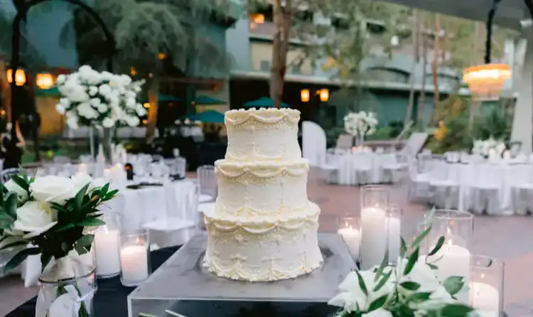 A 3 tier wedding cake with lace piping at an outdoor candlelit reception