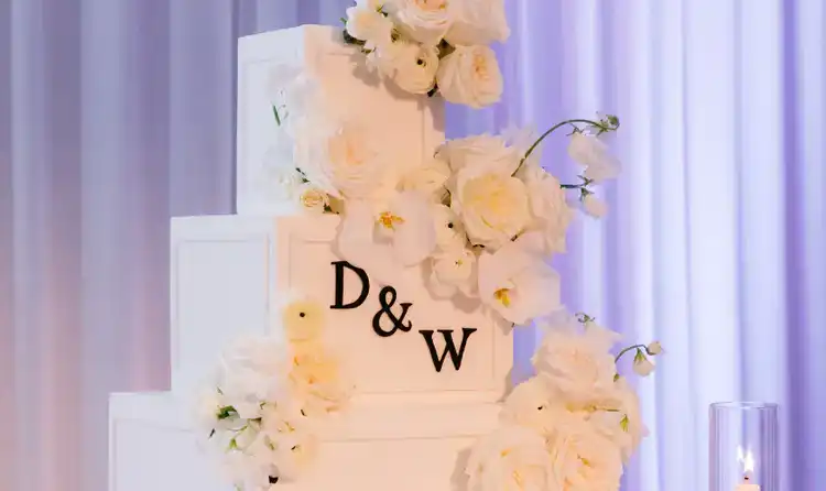 A 4 tier wedding cake monogrammed with the letters D and W, adorned with cream roses and candles