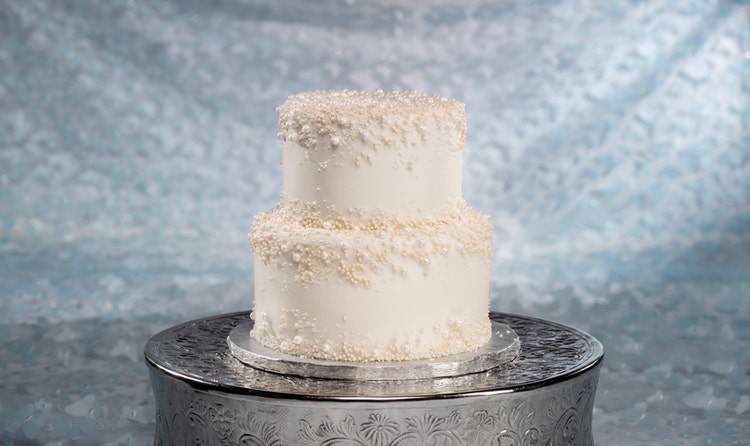 A 2 tier wedding cake adorned with delicate pearl sprinkles around the top edges of each tier