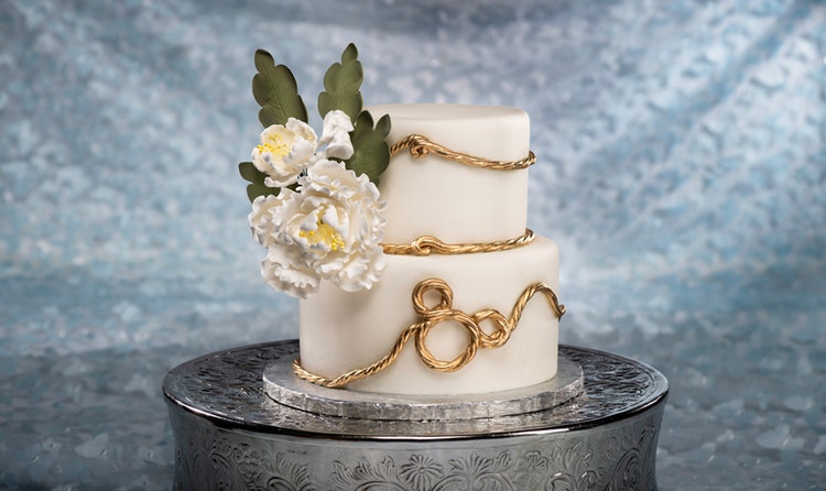 A 2 tier wedding cake adorned with peonies and gold rope