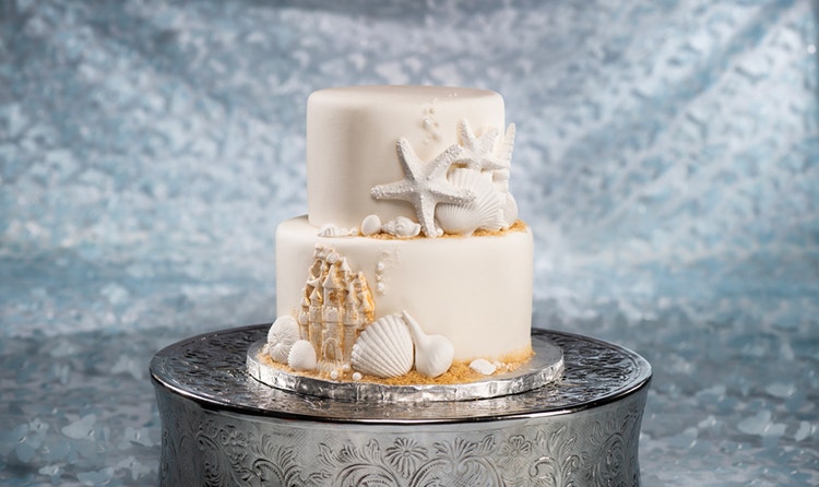 A 2 tier wedding cake adorned with chocolate seashells, starfish and a sandcastle