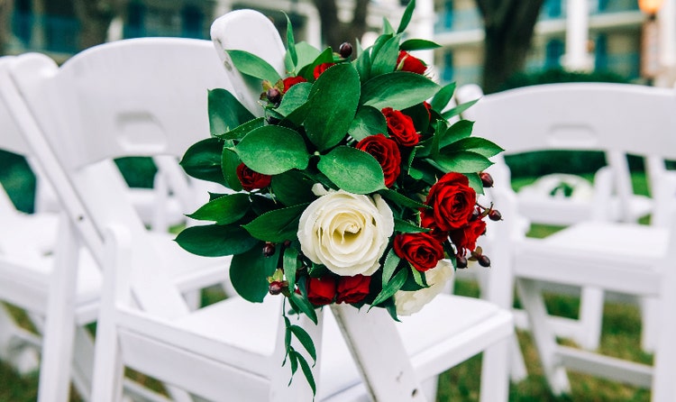 Folding chair decorated with a bouquet of greenery and roses, set up for an outdoor ceremony