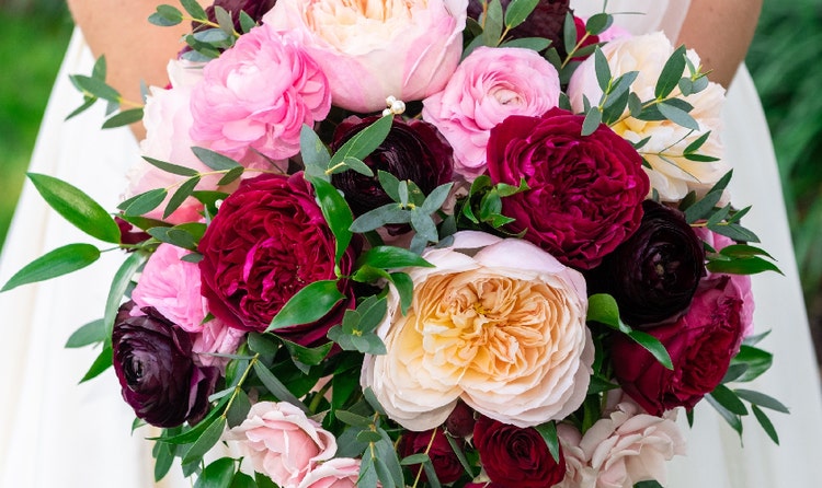 A bride holding a bouquet with peonies and ranuculuses