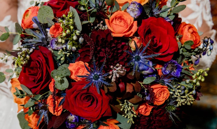 A bride holding with bouquet of roses, dahlias, sea holly and amaranth
