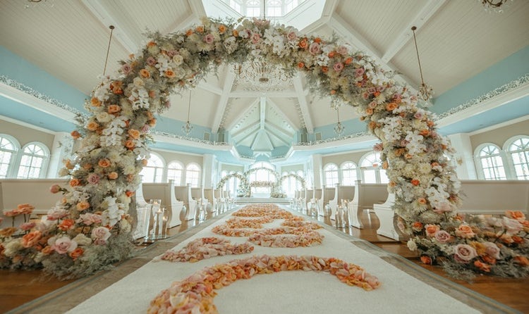 Wedding aisle decorated with flower petals forming a pattern, floral arches and pews inside a chapel