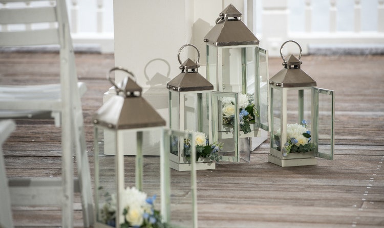Four glass lanterns with floral arrangements on a wooden deck