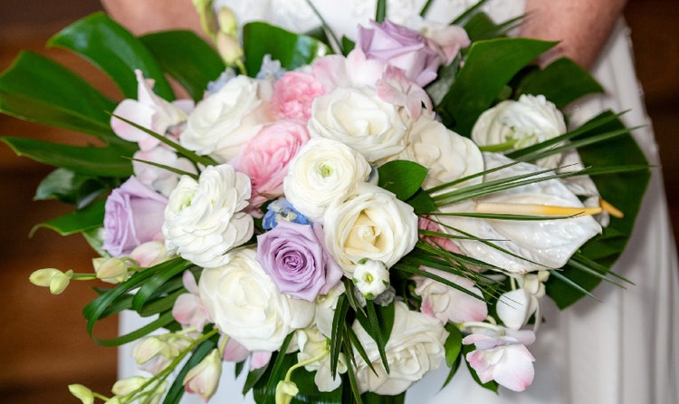 A bride holding a bouquet with roses, peonies, monstera deliciosa and calla lily