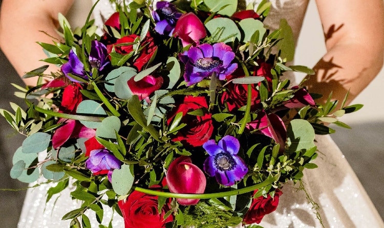 A bride holding a bouquet with roses, calla lilies and anemones
