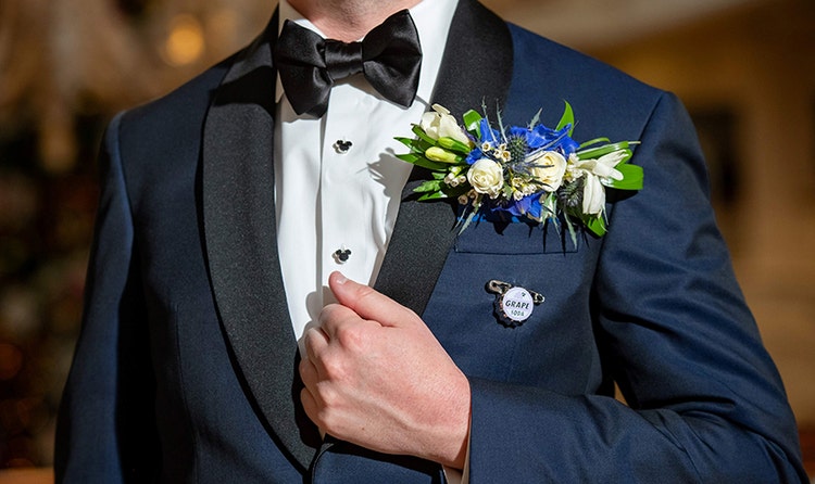 A groom wearing a boutonniere with a mix of roses and other flowers